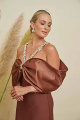 Vestido largo de satén marrón, de corte ajustado al cuerpo, con gran lazo o moña en el escote y tirantes decorados con apliques de pedrería.