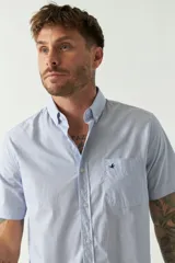 Camisa de manga corta color celeste claro, con cuello abotonado, cierre frontal con botones y bolsillo en el pecho con logo bordado.