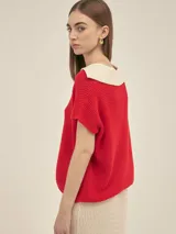 Top tejido color crema, de manga corta, con cuello polo azul marino y corte holgado.