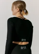 Top deportivo negro de manga larga, tejido de morley sin costuras. Presenta escote cuadrado y tiras finas cruzadas en la espalda.