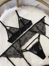 Conjunto de lencería de encaje negro compuesto por un bralette triangular, una tanga y un portaligas integrado. El diseño presenta detalles de encaje floral, breteles regulables y tiras elásticas ajustables.