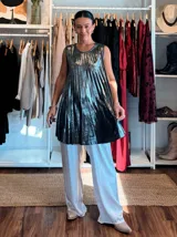 Musculosa de corte amplio y fluido, confeccionada en tejido lamé con acabado metalizado y textura plisada. Presenta un diseño sin mangas con cuello redondo, ideal para eventos nocturnos.