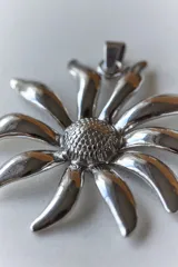 Collar con dije de acero quirúrgico en forma de flor tipo margarita con centro texturizado y pétalos lisos brillantes, montado sobre un tiento largo.