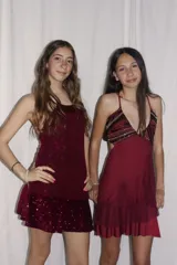Vestido corto de tela metalizada en tono fucsia con reflejos dorados, con escote en V, diseño de top con triángulos, aberturas laterales en la cintura y doble volado irregular en el ruedo.