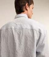 Camisa celeste de viscosa y poliéster con textura arrugada, cuello tradicional, manga larga y abotonadura frontal completa.