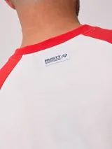 Remera blanca con mangas raglán negras y estampado frontal con el logo de Rusty en azul.