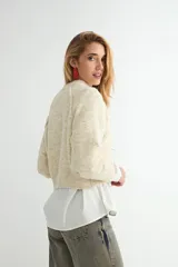 Buzo de tejido de punto con cuello redondo, diseño cropped y mangas largas con puños acanalados. Presenta una textura jaspeada en tono beige.