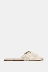 Sandalia plana tipo pala de color beige, con tira ancha decorada con perlas y abalorios brillantes dispuestos en patrón radial, punta redonda y suela plana.