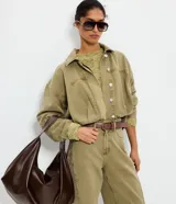 Campera bomber de jean color verde militar, con cuello polo y cierre delantero de botones a presión. Presenta mangas largas abullonadas con puños tejidos en tono contrastante y pliegues que aportan volumen.