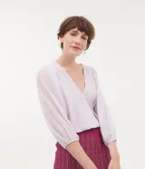 Blusa Cortelle de manga larga en color lila, confeccionada en 100% poliéster. Presenta diseño cruzado (transpasse), escote en V profundo, mangas abullonadas semitransparentes con puños elásticos.