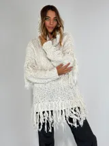 Sweater con capucha color crudo, de tejido grueso con flecos en las mangas y el dobladillo.