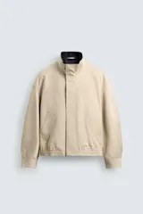 Cazadora regular fit de algodón color beige, con cuello subido y forro interior a cuadros. Presenta cierre frontal de cremallera oculta por solapa con botones a presión, bolsillos de vivo en la cadera y puños con botón.