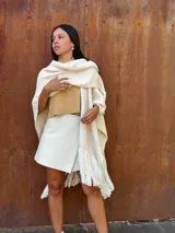 Ruana tejida de lana en color crudo, con diseño de flecos en los bordes. Es una prenda versátil y abrigada, ideal para complementar diversos looks.