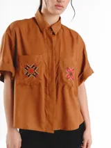 Camisa de manga corta color amarillo claro, con calce oversized, hombros caídos y cierre frontal con botones. Cuenta con bolsillos delanteros con bordados geométricos y mangas con dobladillo.