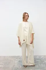 Ruana tejida en color crudo, de corte abierto y diseño holgado, con detalle de etiqueta de cuero en el frente.