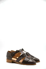 Zapato tipo cangrejera de cuero color marrón, con diseño de tiras entrelazadas, punta cerrada y pulsera con hebilla ajustable al tobillo. Cuenta con un taco bajo de madera.