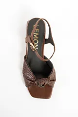 Sandalias de cuero marrón con taco cuadrado medio, tira en el tobillo con hebilla ajustable y diseño trenzado con nudo en la parte delantera.