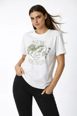 Remera de algodón blanca con cuello redondo y mangas cortas. Presenta un estampado frontal en tonos verdes con forma de corazón, rosas, texto y detalles de strass.