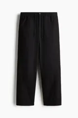 Pantalón en mezcla de algodón color negro, con cintura elástica con cordón de ajuste y botón. Presenta bolsillos laterales discretos y costuras giradas en las piernas, con un corte relajado.