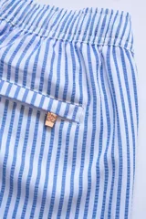 Short de baño celeste con rayas verticales blancas, cintura elástica con cordón ajustable, bolsillos laterales y trasero con cierre, logo de la marca bordado en la pierna.