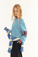 Remera de manga larga con corte boxy, confeccionada en algodón. Presenta un diseño de rayas horizontales en tonos azul y fucsia, con detalles de rayas verticales en los codos, tajos laterales y logo bordado en el pecho.