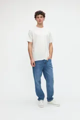 Remera de manga corta color blanco off-white, de calce clásico en tejido jersey de algodón. Presenta un gran diseño estampado en la espalda con un recuadro celeste que incluye las leyendas "WILD OCEAN" y "SALTY SOUL" junto con gráficos de olas y estrellas en tonos rosados y amarillos.