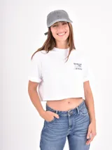 Remera blanca de corte crop, con mangas cortas con dobladillo y estampa pequeña en el pecho con texto en color azul.
