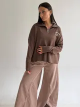 Sweater de tejido bremer color blanco, con cuello polo, cierre frontal y bordado en el pecho. Presenta mangas largas y diseño de corte holgado con terminaciones acanaladas.