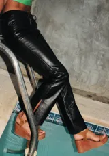 Pantalón de cuero color marrón con estampado abstracto, corte acampanado y abertura en el ruedo.