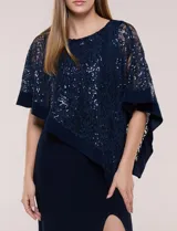 Vestido largo azul marino de seda fría, compuesto por una falda recta con tajo frontal y una capa superior superpuesta de encaje con lentejuelas bordadas, escote a la base y mangas tres cuartos acampanadas.