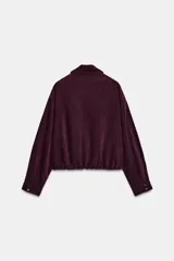 Cazadora bomber de Zara, de color bordó, con cuello de solapa, manga larga, bolsillos de vivo en el delantero y bajo elástico. Cuenta con cierre frontal de cremallera metálica.