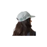 Gorra Eme Studios color gris claro con visera plana y bordado en relieve verde oscuro con borde blanco en el frente.