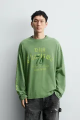 Camiseta de manga larga con corte relajado y cuello redondo, confeccionada con un acabado de efecto lavado. Presenta un estampado frontal con tipografía gótica y números en contraste.