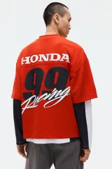 Remera de malla color rojo, con cuello en V, mangas cortas y corte oversized. Cuenta con diseño estampado frontal de Honda con banderas a cuadros y el logo de la marca.