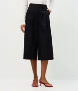 Pantalón pantacourt de sastrería con diseño amplio, cintura alta y pliegues frontales. Presenta piernas anchas, largo midi y cierre frontal discreto.
