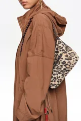 Bolso de hombro mini Bimba Y Lola con estampado animal print tipo leopardo, cierre superior con cremallera y bolsillo exterior con cierre. Presenta detalles de cordones con cuentas rojas y tiras colgantes en el lateral.
