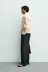 Cazadora boxy fit color beige, confeccionada en tejido de algodón y lino. Presenta cuello solapa, manga larga con puño abotonado, bolsillos de vivo en la cadera y bajo con elásticos laterales. Cierre frontal de botonadura.