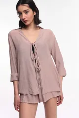 Camisa color beige con textura arrugada, escote en V profundo con cordones ajustables y mangas largas con puños doblados.