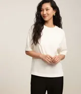 Blusa básica de mujer color negro, confeccionada en malla encorpada de algodón, con cuello redondo y mangas cortas de corte oversized con sisas desplazadas.