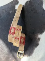 Cinto de cuero marrón claro con detalles bordados geométricos en tonos azul, rojo y beige, hebilla metálica de bronce y puntera forrada en cuero.