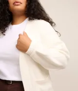 Cardigan abierto de punto color blanco, con mangas largas abullonadas, bolsillos delanteros y diseño alargado.