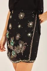 Falda corta cruzada con diseño envolvente y lazo lateral para ajuste. Presenta bordados florales detallados en toda la superficie, tanto en el frente como en la espalda. Está completamente forrada para mayor comodidad.