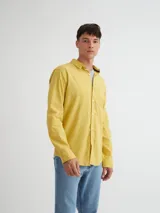Camisa manga larga amarilla de algodón con bolsillo en el pecho, botones de pasta, logo bordado en el ruedo y etiqueta de marca en la tapeta de botones.