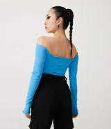 Blusa cropped de media malla color celeste, con escote hombro a hombro, mangas largas con abertura para los dedos y volantes en el escote, puños y bajo.