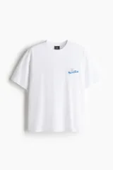 Remera blanca de algodón con cuello redondo y mangas cortas, corte holgado y pequeño estampado azul en el pecho con la inscripción "Sevilla".