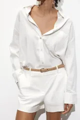 Bermuda de tiro medio color azul marino, con pinzas delanteras, cierre frontal y cinturón fino color beige.