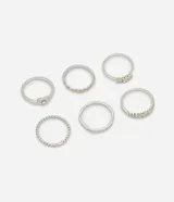 Set de seis anillos de metal plateado con diversos diseños, incluyendo modelos lisos, texturizados, trenzados, uno con dije de corazón y otro con incrustaciones de zirconia.