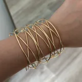 Pulsera rígida dorada con diseño geométrico de líneas entrecruzadas.