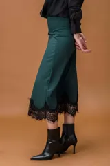 Falda midi de satén en color verde oscuro, con corte irregular y detalle de encaje negro en el ruedo y en uno de los laterales.