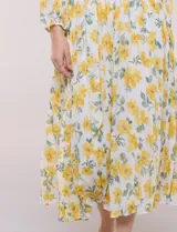 Vestido maxi de gasa con estampado floral en tonos amarillos y verdes sobre base blanca, escote en V cruzado, mangas largas y cintura elastizada con lazo.